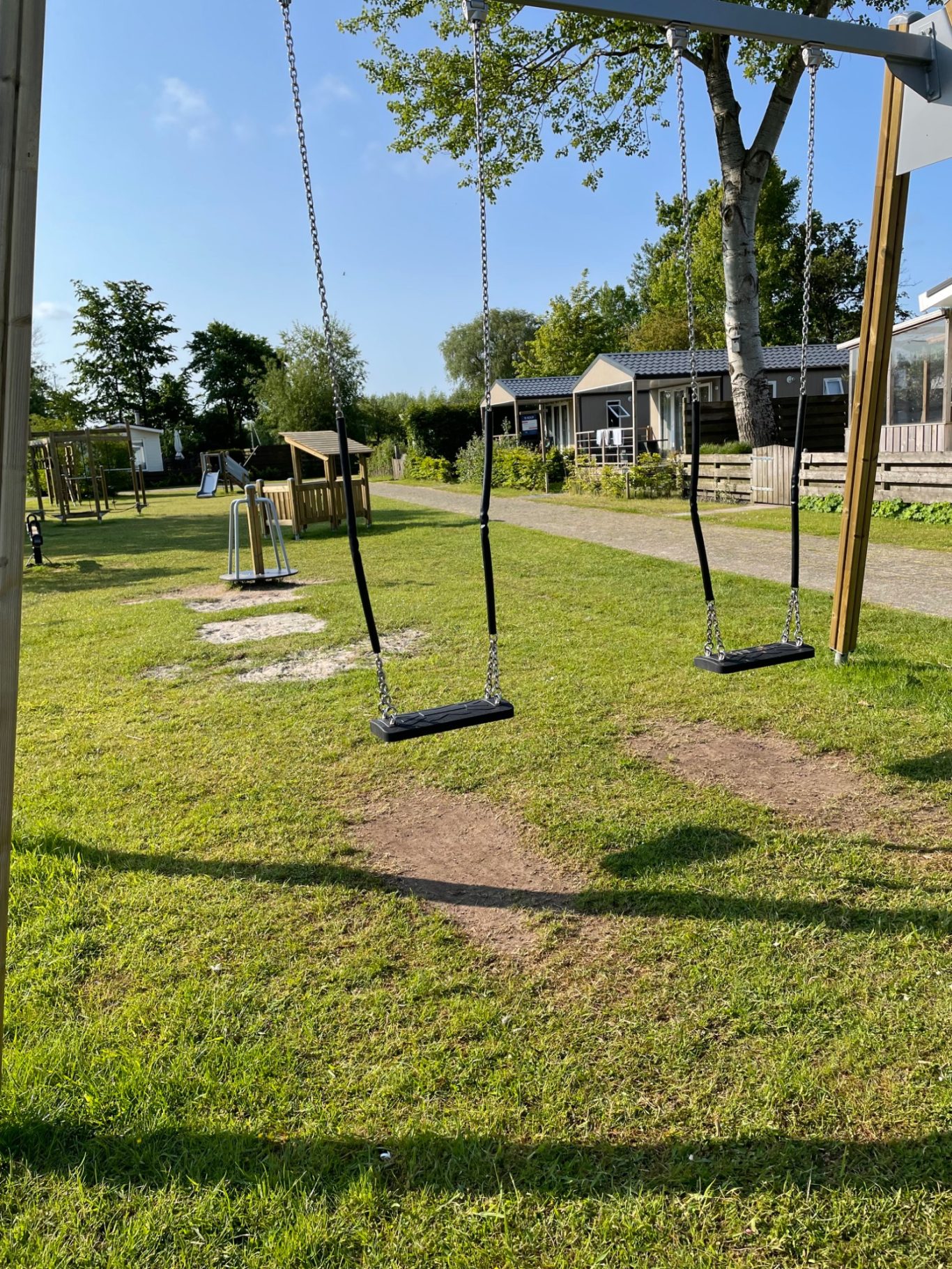 Spielplätze Schaukelplatz mit mehreren Schaukeln und grünem Rasen im Hintergrund.