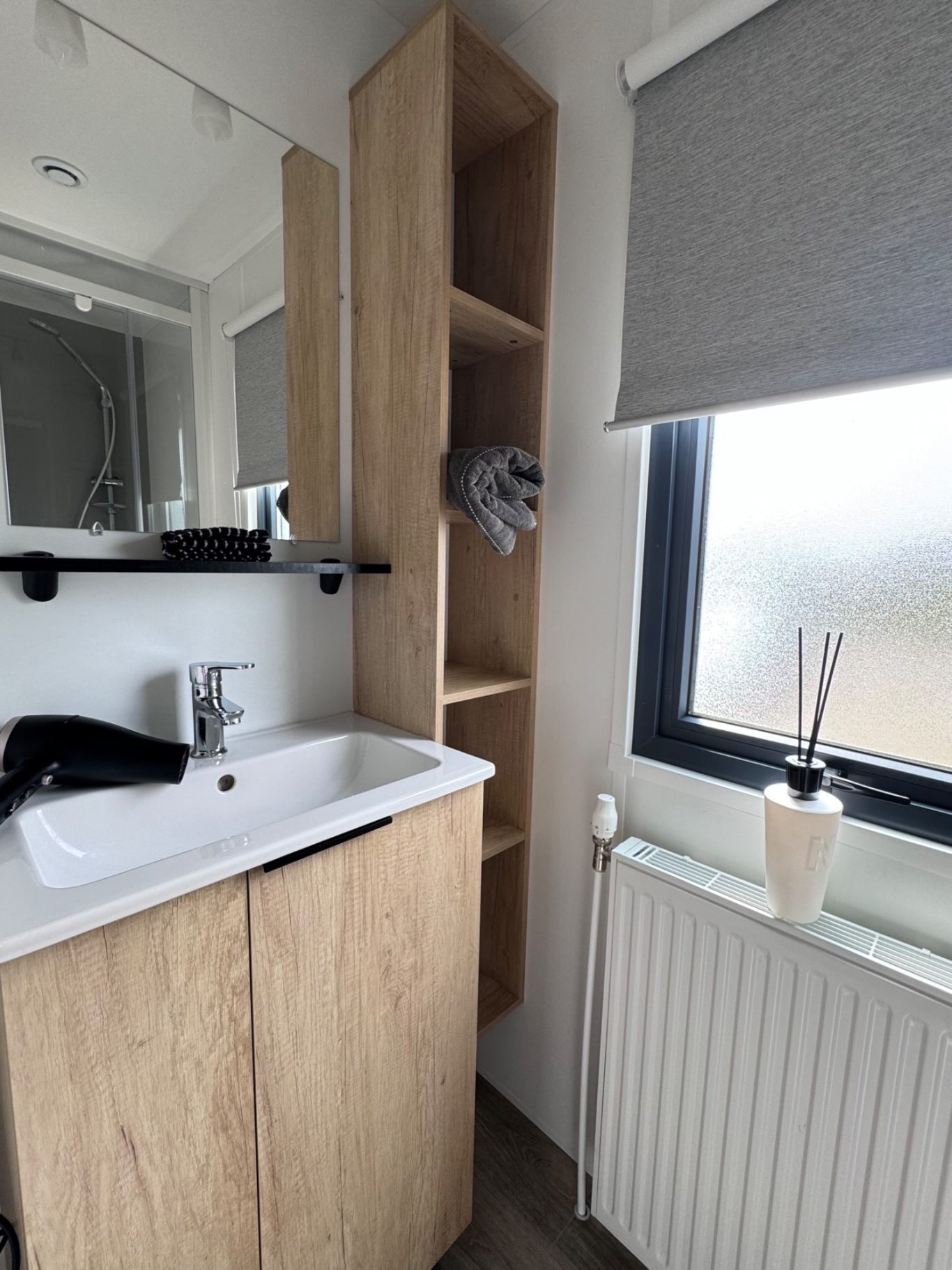Badezimmer Helles Badezimmer mit Waschbecken, Holzregal und Deko an der Fensterbank.