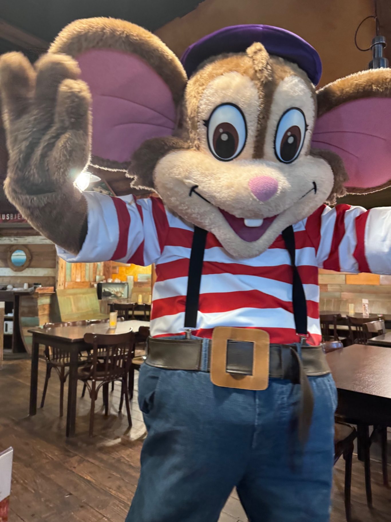 Kinderanimation Ein fröhliches Maskottchen mit großen Ohren, gestreiftem Shirt und blauer Hose.