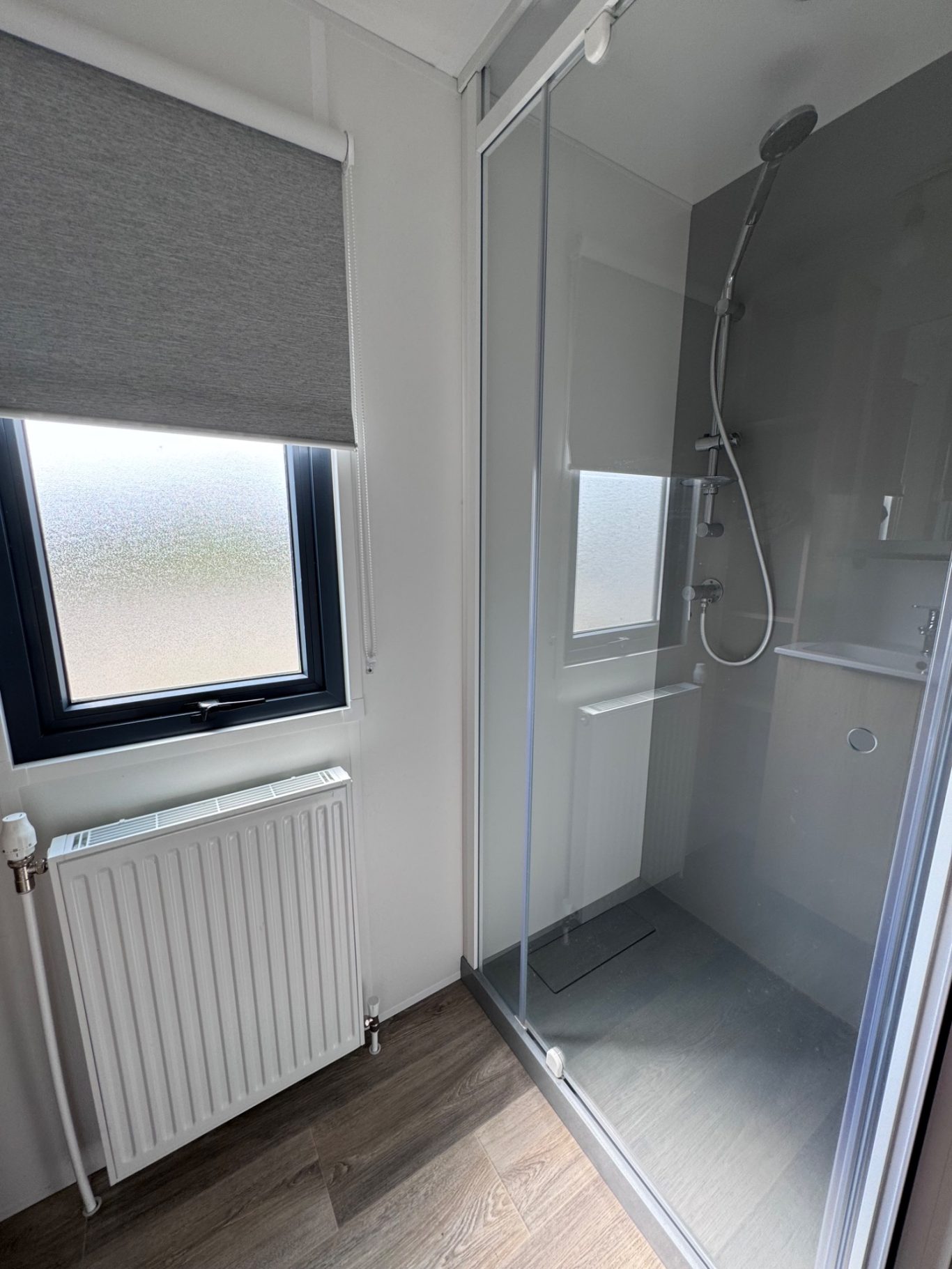 Badezimmer Moderne Dusche mit klaren Glasschwingtüren, Fenster und Heizkörper im Raum.