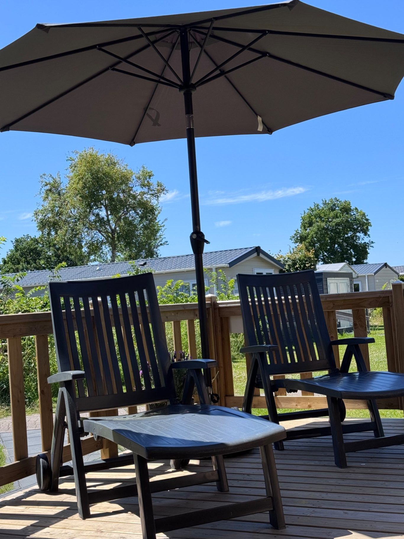Terrasse Zwei schwarze Liegestühle unter einem Sonnenschirm auf einer Terrasse mit Blick ins Grüne.