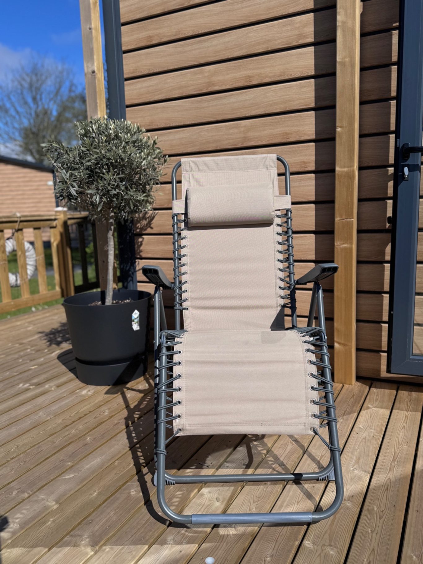 Terrasse Ein beiger Liegestuhl steht auf einer Holzterrasse neben einem Pflanzkübel.