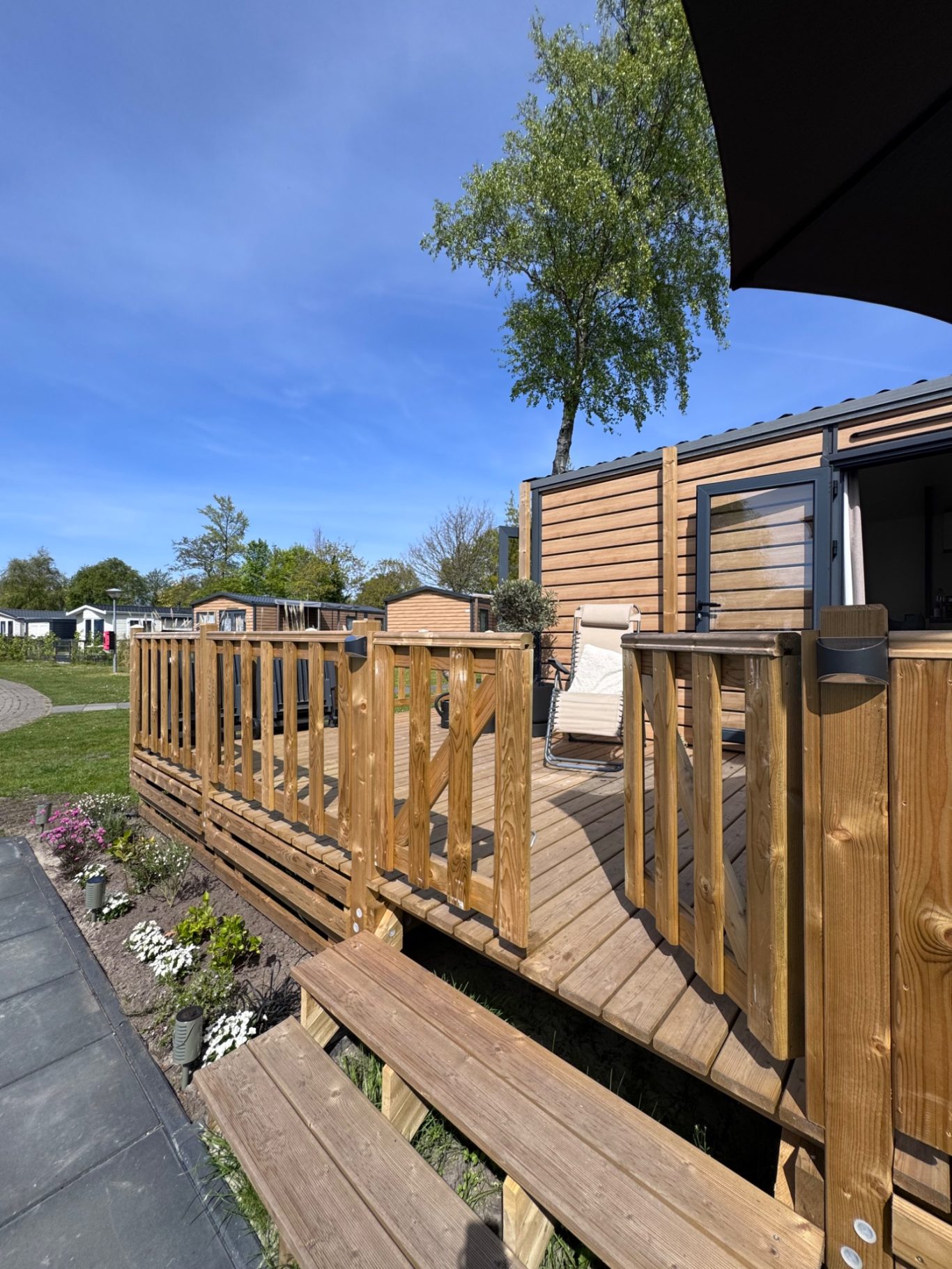 Terrasse Holzterrasse mit Geländer und Gartenpflanzen unter blauem Himmel.