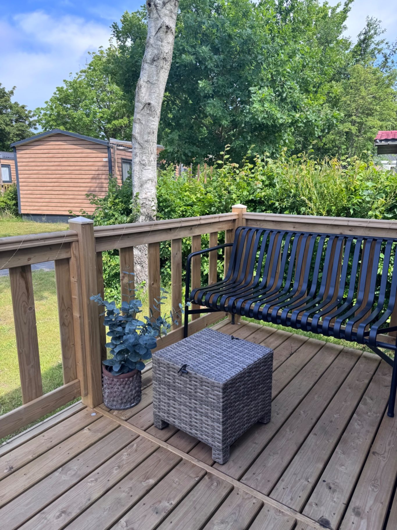 Terrasse Holzbodenveranda mit einer Bank, einem Hocker und einem Blumentopf vor einem grünen Hintergrund.