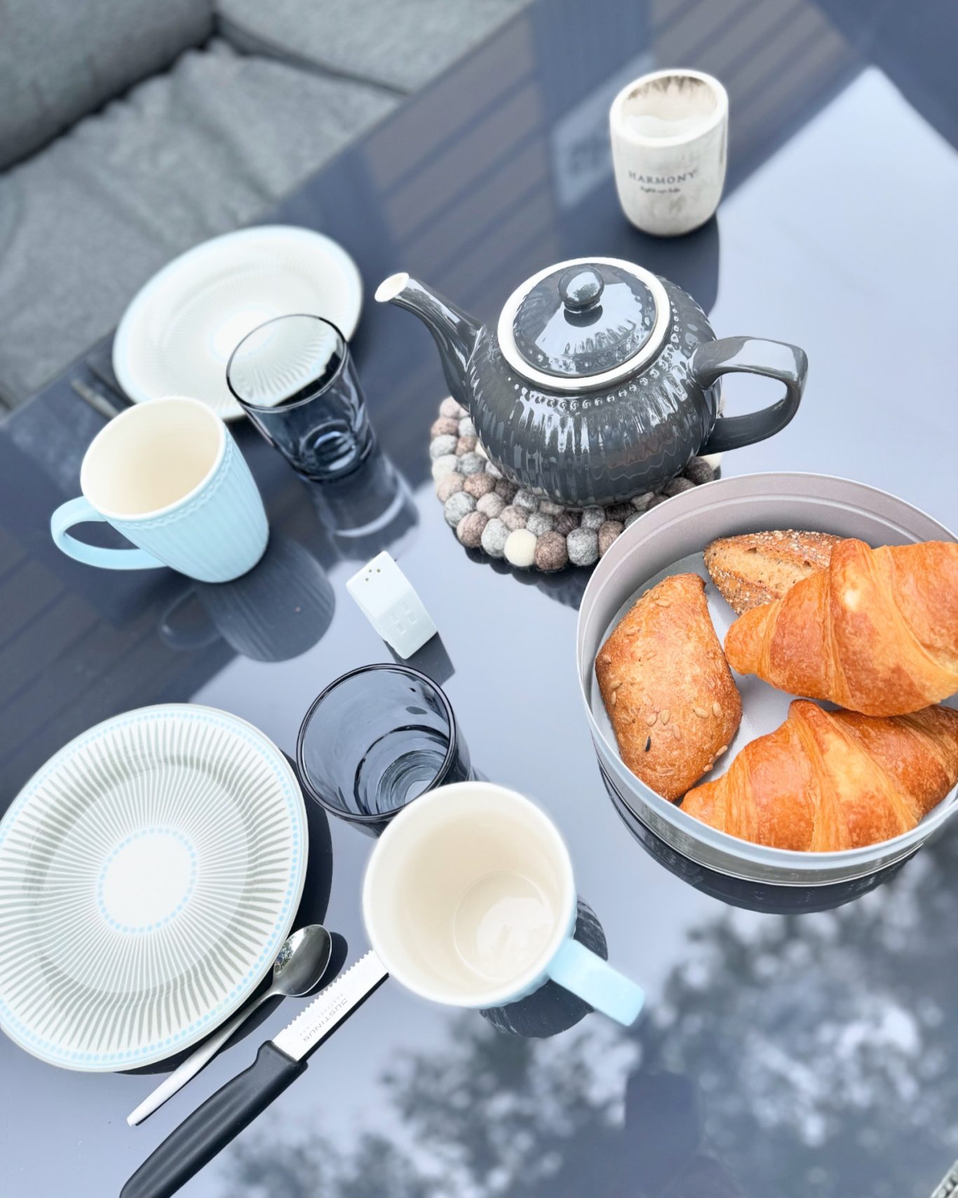 Geschirr Tischgedeck mit Teekanne, Tellern, Gläsern und einer Schüssel mit Croissants.