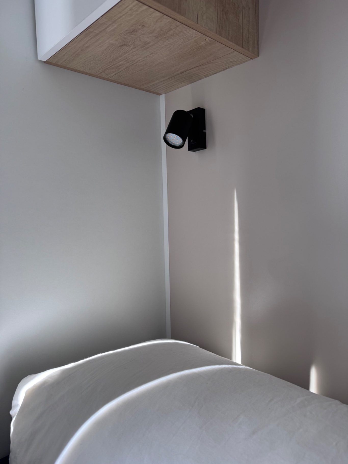 Schlafzimmer 2 Eine Wandlampe in einer Ecke neben zwei gestapelten Kissen auf einem Bett.
