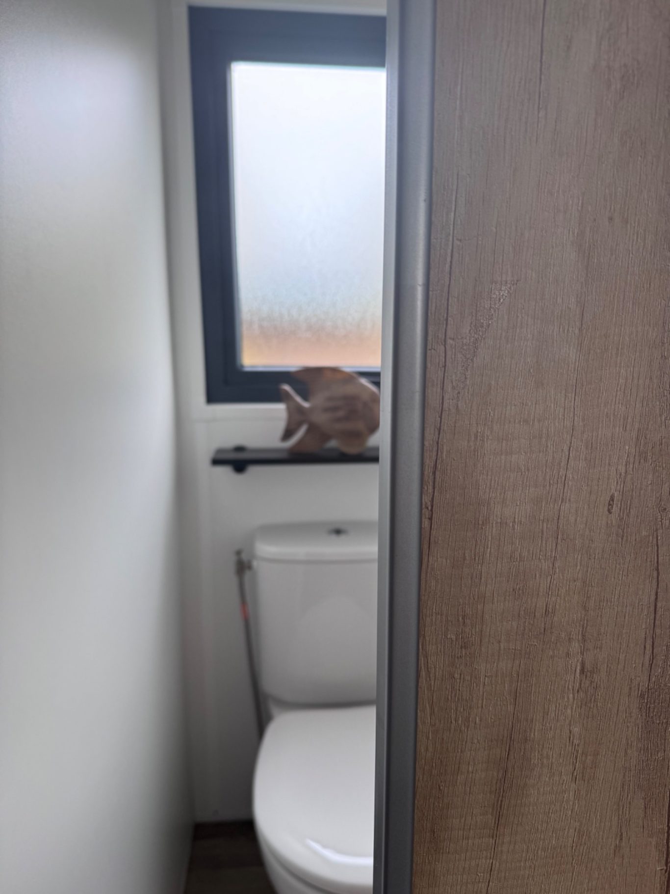 Toilette bei Hauptschlafzimmer Ein kleines, schlichtes Badezimmer mit einer Toilette und einem Fenster.