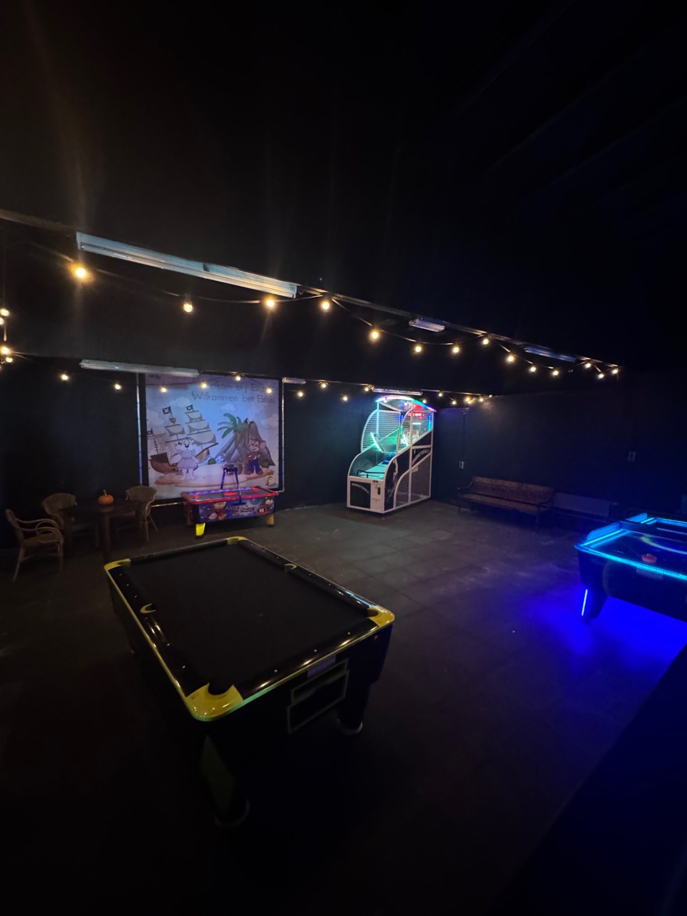 Spielecenter Dunkler Raum mit Billardtisch, Spielautomaten und Lichtern.