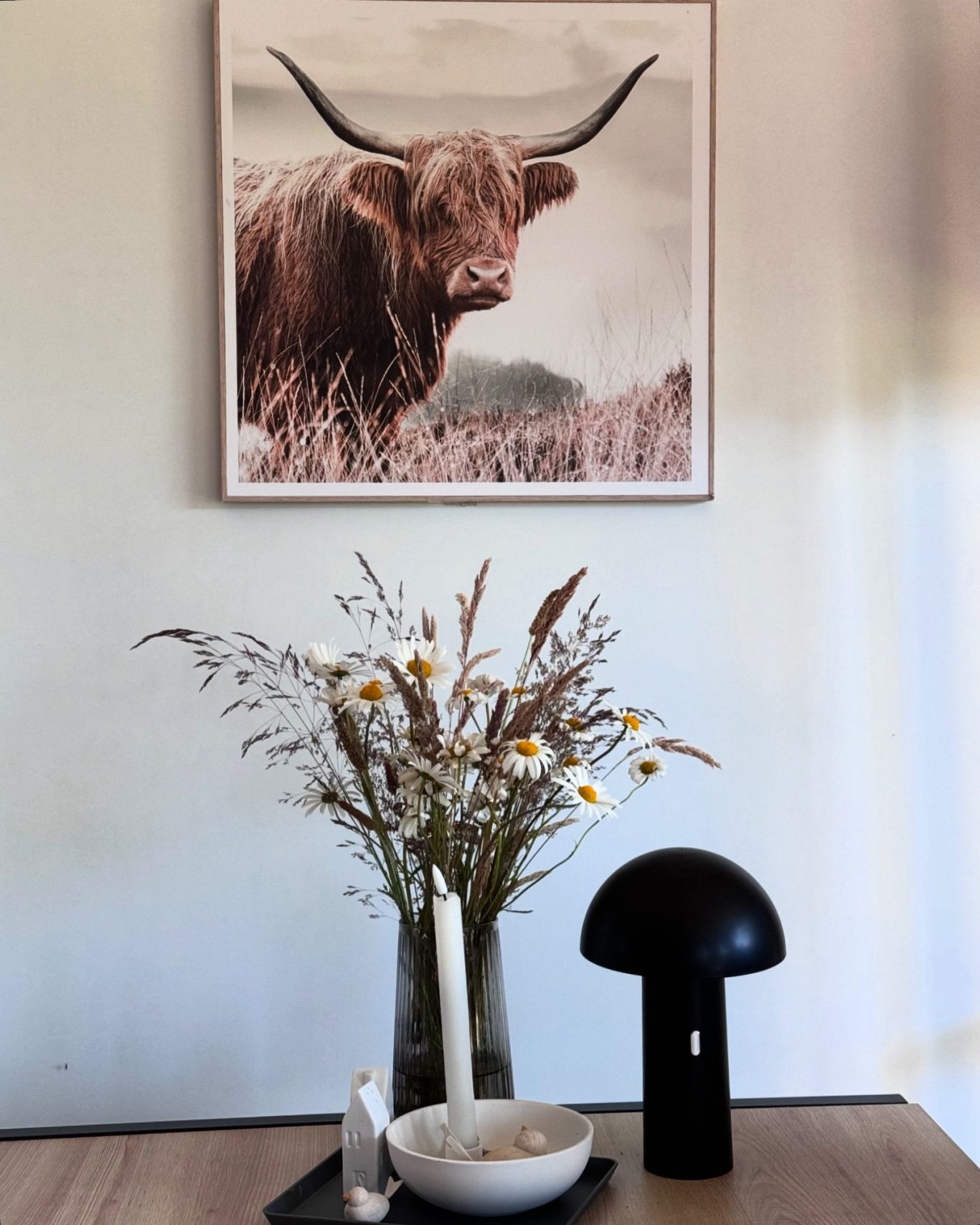 Einrichtungdetailles Ein Hochlandrind auf einem Bild über einer Vase mit Trockenblumen und einer Lampe.